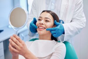 Woman in dental chair looking at her finalized cosmetic dental procedure in a mirror.